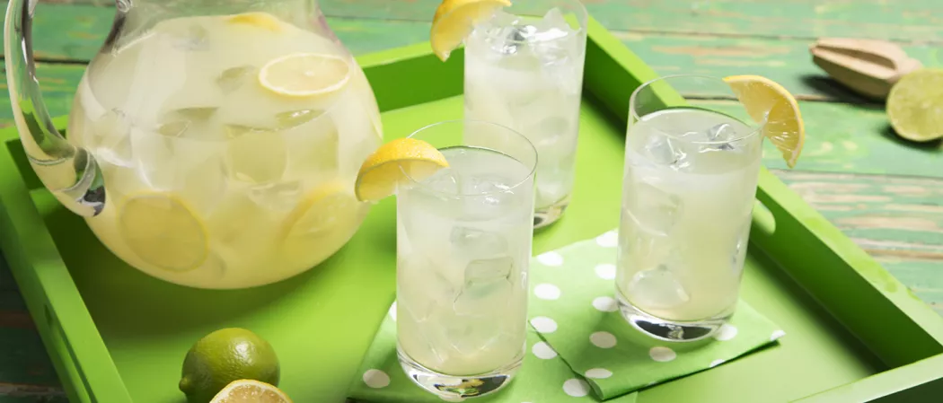 Three glasses of Limonlicious garnished with Lemon Wedge and a jar of Limonlicious  along with  chopped lemons and a sqeezer on the table