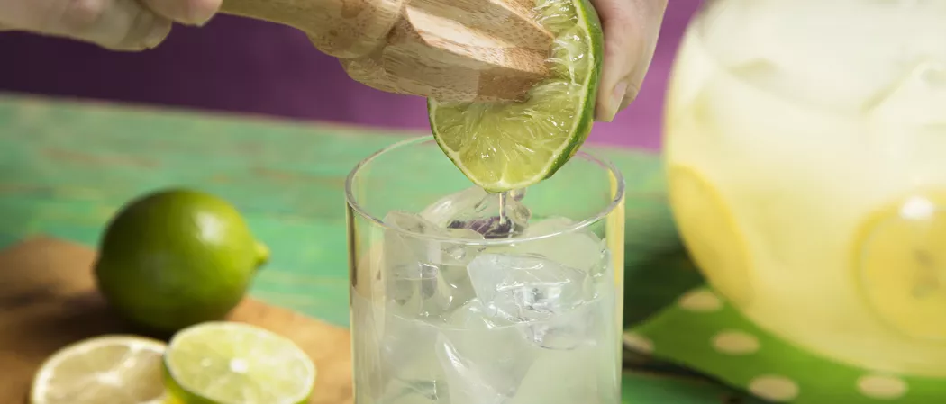 A person sqeezing a lemon itno the glass of Limonlicious cocktail with the help of citrus zester