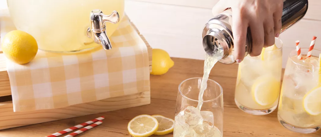 Person pouring Vodka Lemonade from a shaker into glass filled with ice