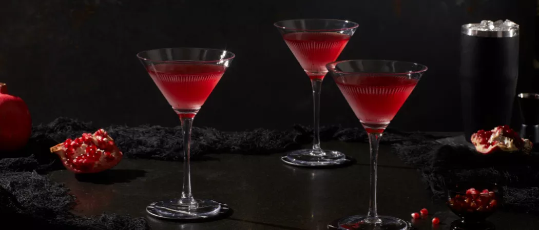 Three glasses of Pinnacle® Black Widow Martini alongside pomegranate