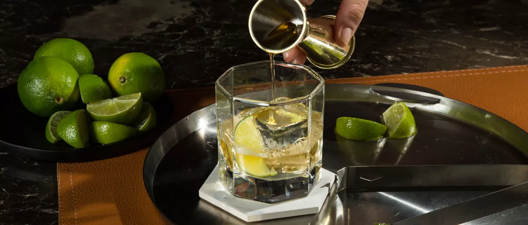 A person pouring Fever-Tree Ginger Ale into a glass of CC® Ginger Ale along with chopped lemons