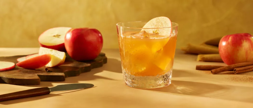 A glass of SQRRL® An Apple A Day garnished with Fresh Apple Slices and Cinnamon along with chopped and unchopped apples
