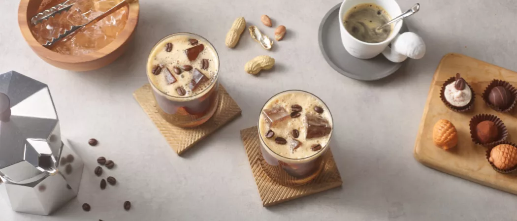 Two glasses of SQRRL® Carajillo garnished with Coffee Beans along with some ground nuts and a jar of coffee beans on a kitchen slab