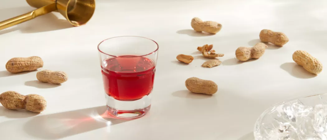 A glass of SQRRL® PB&J Shot along with some ground nuts on the kitchen slab
