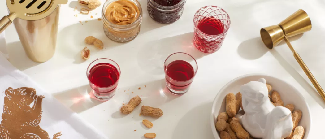 Three glasses of SQRRL® PB&J Shot along with the cocktail shaker, howthrone, bowl of groundnuts and a glass of SQRRL® Peanut Butter Whiskey
