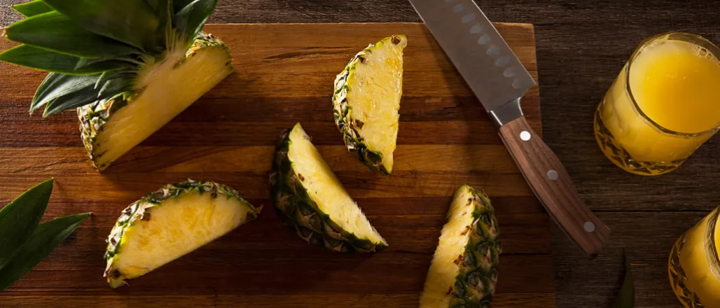 Pineapple slices knife on wooden tray and a glass of Pequeña Colada on a wooden table