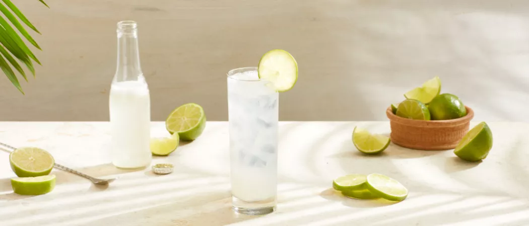 A glass of Sauza® Mexican Paloma garnished with Lime Wheel along with a bottle of Grapefruit Soda  and a bowl of lemons