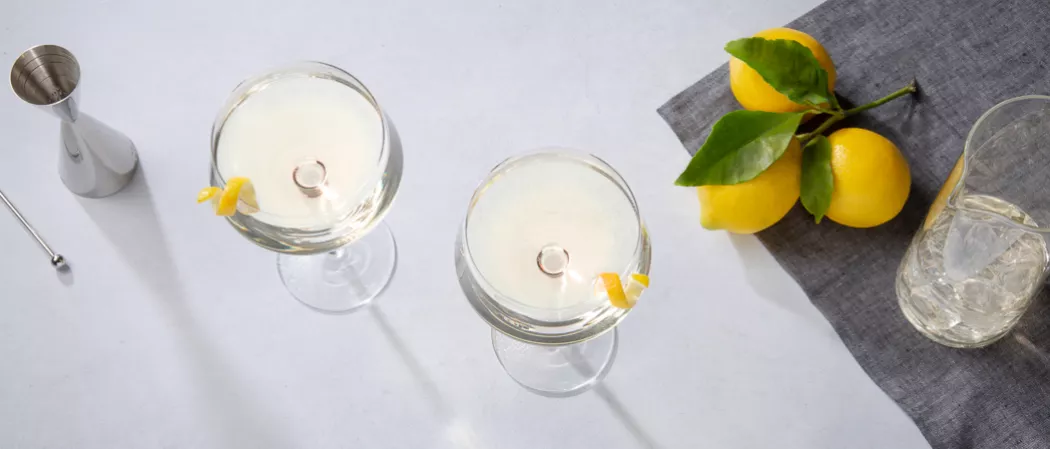 Two glasses of Vesper garnished with lemon peel along with the jiggern a steel spoon a  jug of ice cubes and lemons