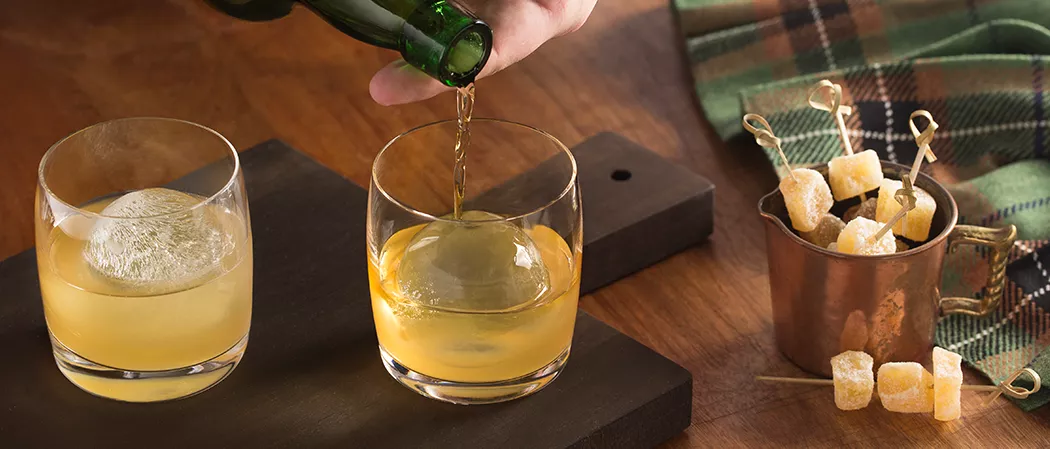 Personn pouring Laphroaig® Penicillin into glass alongside another glass of Laphroaig® Penicillin and mug filled with candies ginger