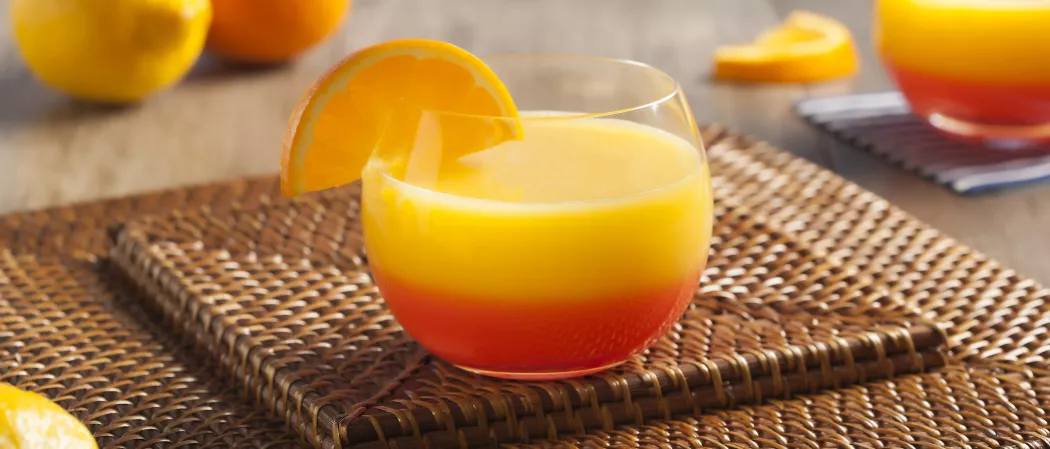 A glass of Sunrise granished with lemon slice sits on the coaster.