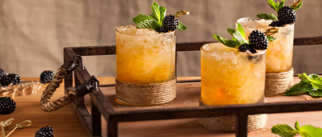 Three glasses of Hats Off Julep on a wooden tray garnished with blackberries.