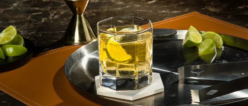 A glass of CC® Ginger Ale garnished with Lime Wedge along with chopped lemon in the plate on a table