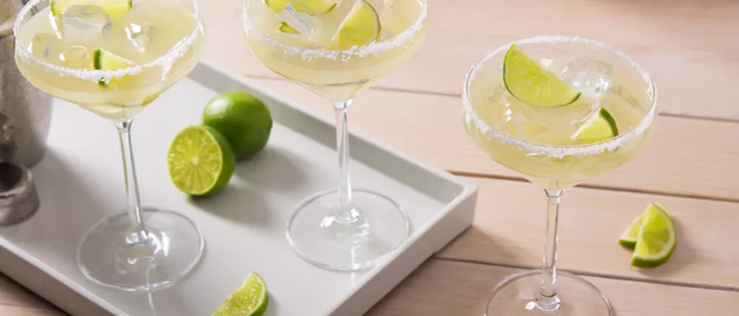 Three glasses of Sauza® Classic Margarita garnished with lemon slices and salt, two on white tray alongside few lime slices