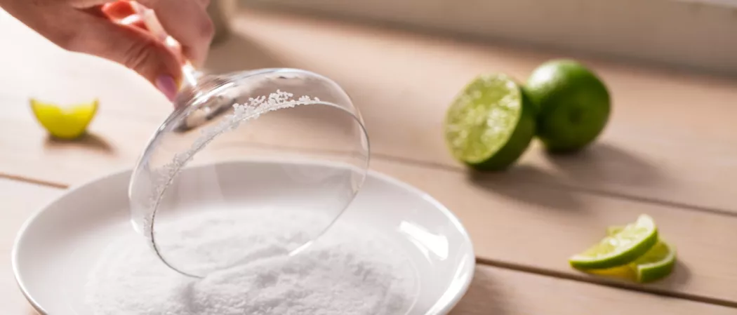 A person rimming a glass with salt alongside a lime and few lime slices