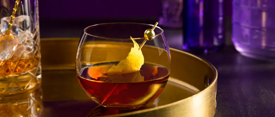 Glass of Courvoisier® Classic garnished with lemon peel on a steel tray