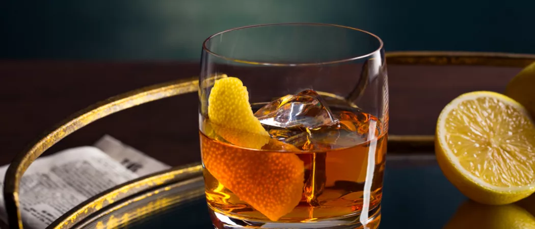 Glass of Dry Rye Manhattan garnished with lemon peel alongside half lemon