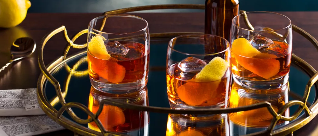 Three glasses of Dry Rye Manhattan garnished with lemon peel alongside half lemon