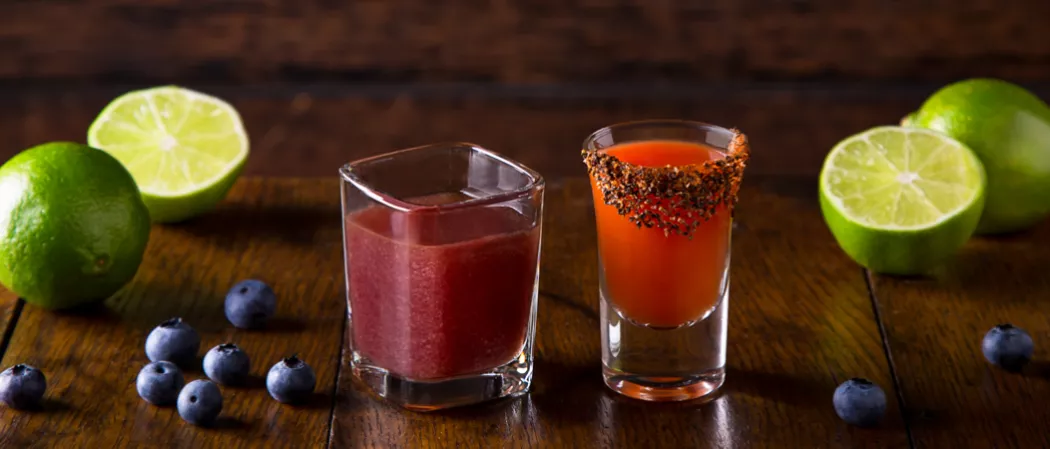 Glass of Stars Bloody Mary alongside glass of Stripes Bloody Mary, some blueberries and limes