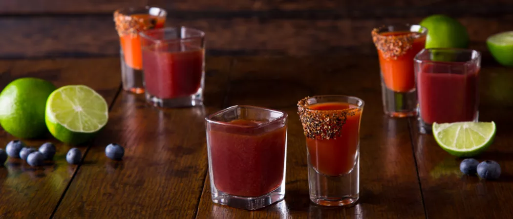 Three Glasses of Stars Bloody Mary alongside three glass of Stripes Bloody Mary, some blueberries and limes