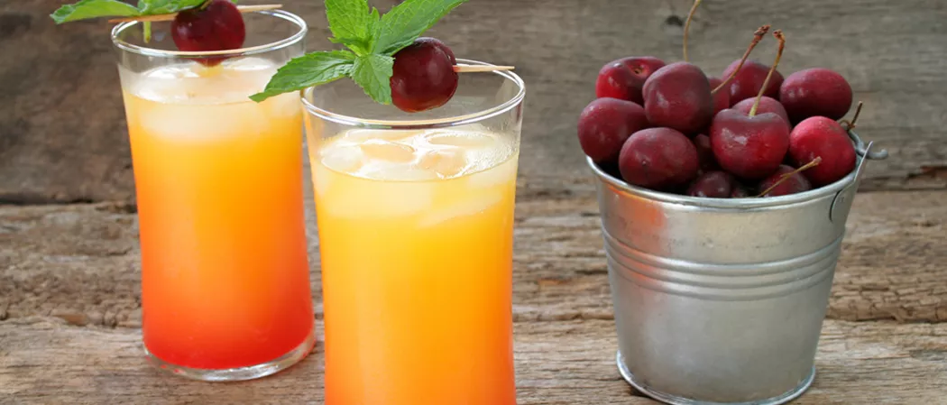 Two glasses of Cruzan® 9 Punch garnished with cherry and mint leaves alongside bucket of cherries
