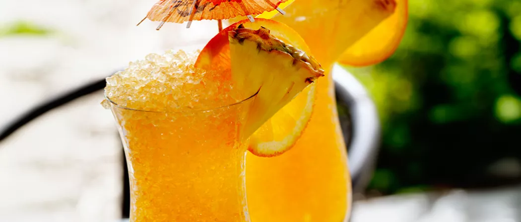 A glass of Classic Rum Punch garnished with crushed ice, orange and pineapple slices, and a cocktail umbrella on the rim of the glass.
