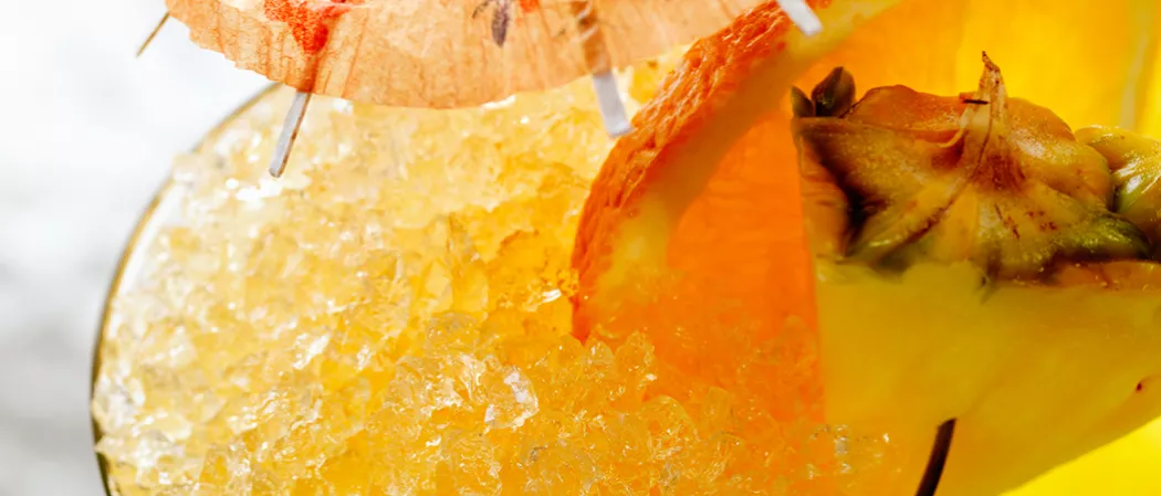 A glass of Classic Rum Punch garnished with crushed ice, orange and pineapple slices, and a cocktail umbrella on the rim of the glass.