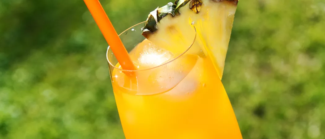 A glass of Classic Rum Punch garnished with ice cubes, a pineapple slice on the rim, and a straws.