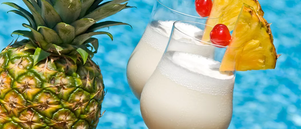 Two glasses of Cruzan® Colada garnished with pineapple slice and cherry alongside a pineapple