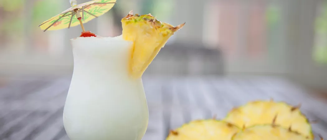 Two glasses of Cruzan® Colada garnished with pineapple slice, cherry and cocktail umbrella alongside few pineapple slices