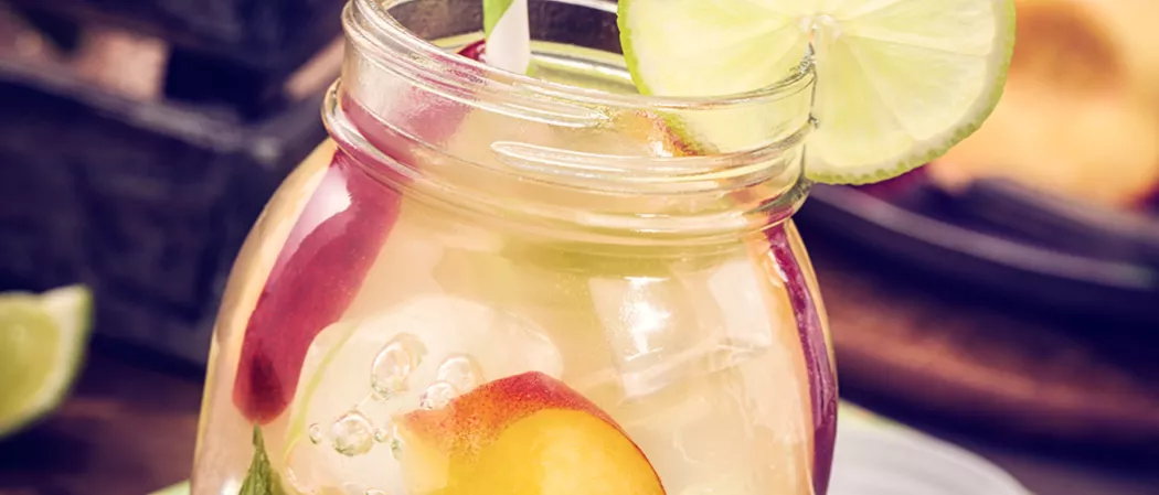 A jar of Peach Daiquiri garnished with lime slice, peach slices and a straws