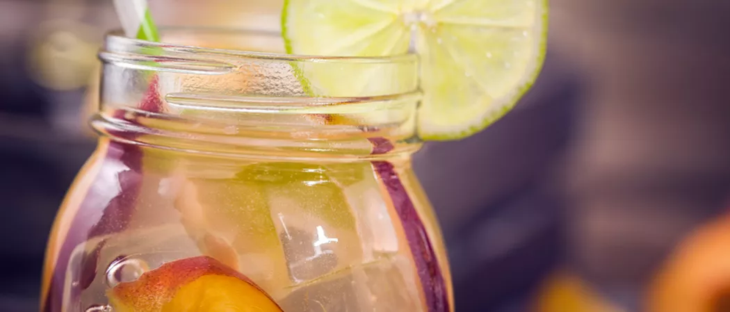 A jar of Peach Daiquiri garnished with lime slice, peach slices and a straws