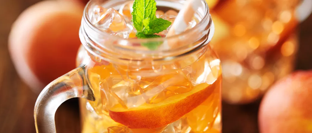 A Glass of Peach Mojito garnished with a mint sprig and a peach slice, with some ice cubes in it.