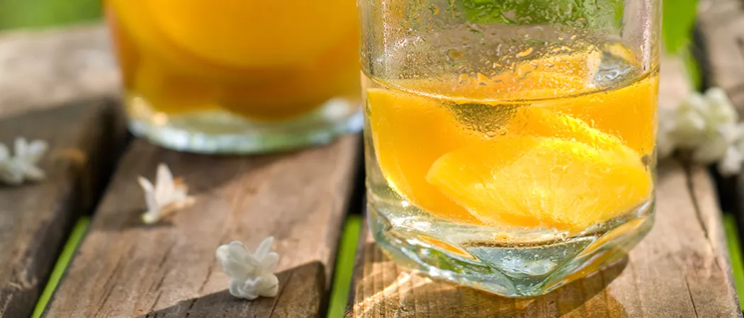 A glass of Cruzan® Peach Sangria, with some jasmine flowers and its leaves spread on the wooden bench.