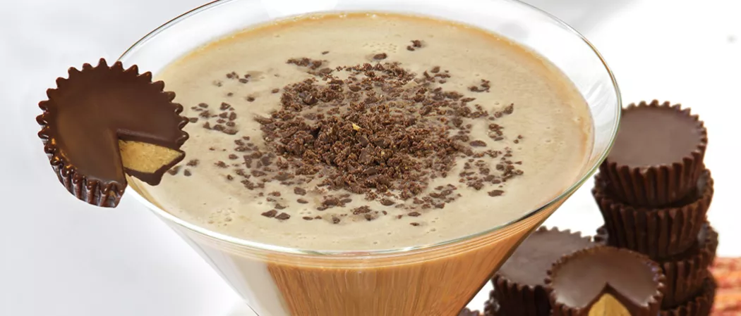 Glass of Peanut Butter Cup Martini garnished with Peanut Butter Cup alongside few Peanut Butter Cups 