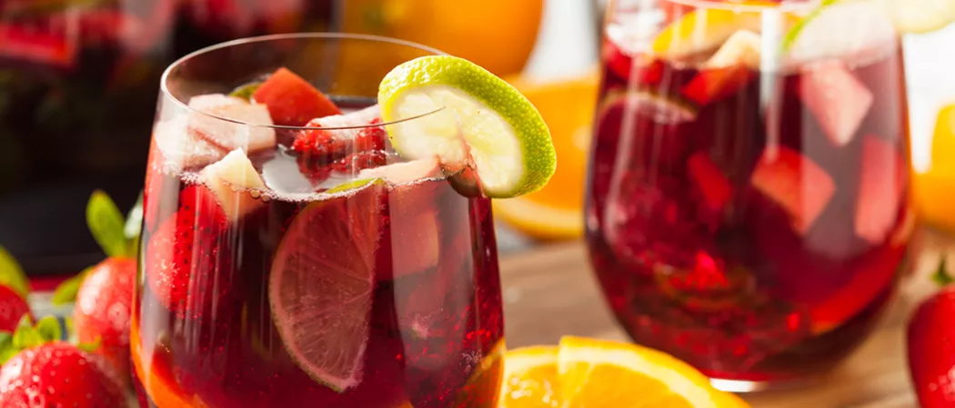 Two glass of Razzmatazz® Sangria garnished with  chopped fruits and a lemon slice on a rim.