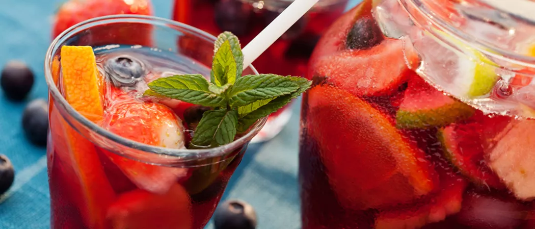 Glass and jar of Razzmatazz® Sangria Garnished with chopped fruits , mixed berried and a straws