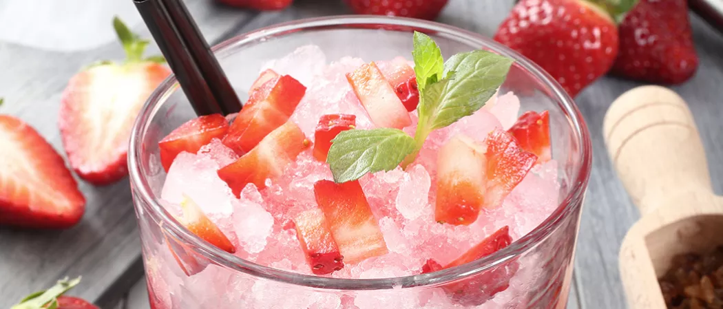 Glass of strawberry Margarita garnished with crushed ice, strawsberry pieces, mint leaves and straws