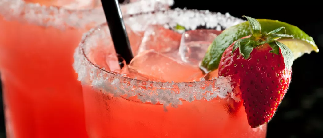 Rimmed glass of strawsberry Margarita garnished with strawsberry and lemon wedge