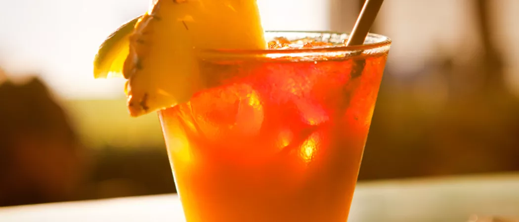 A glass of Watermelon Mai Tai, garnished with ice cubes, orange and pineapple slice on the rim of the glass, and a straws
