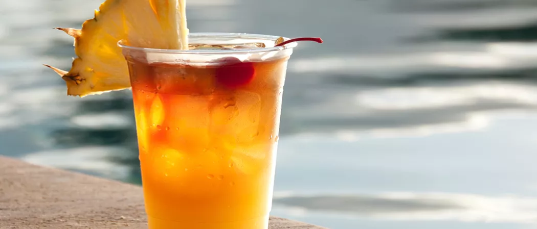 A glass of Watermelon Mai Tai, garnished with ice cubes, cherry and a  pineapple slice on the rim of the glass