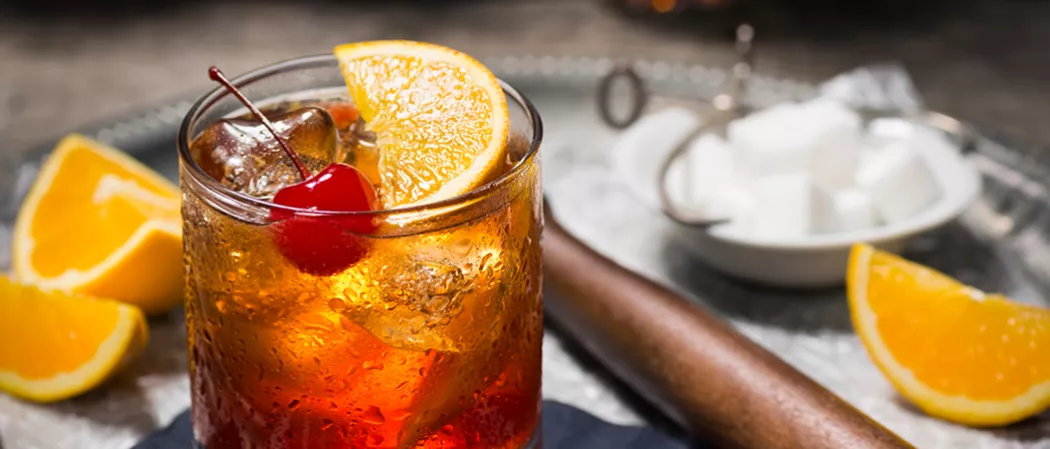 a glass of Bourbon Cider Cocktail drink garnished with ice and a slice of orange