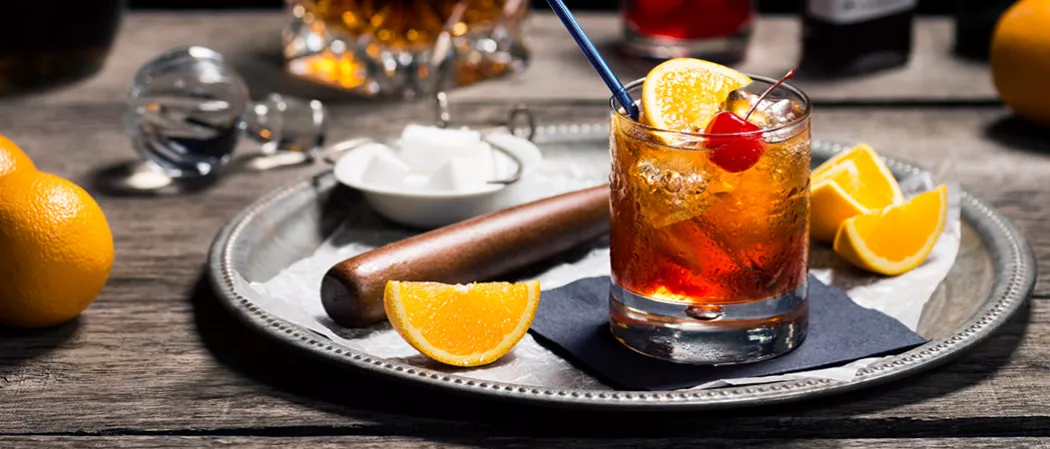 a glass of Bourbon Cider Cocktail  garnished with orange slices and a rolling pin