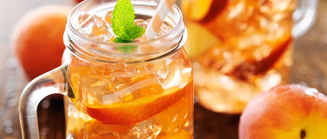 Glass of peach tea garnished with mint leaves and a straws