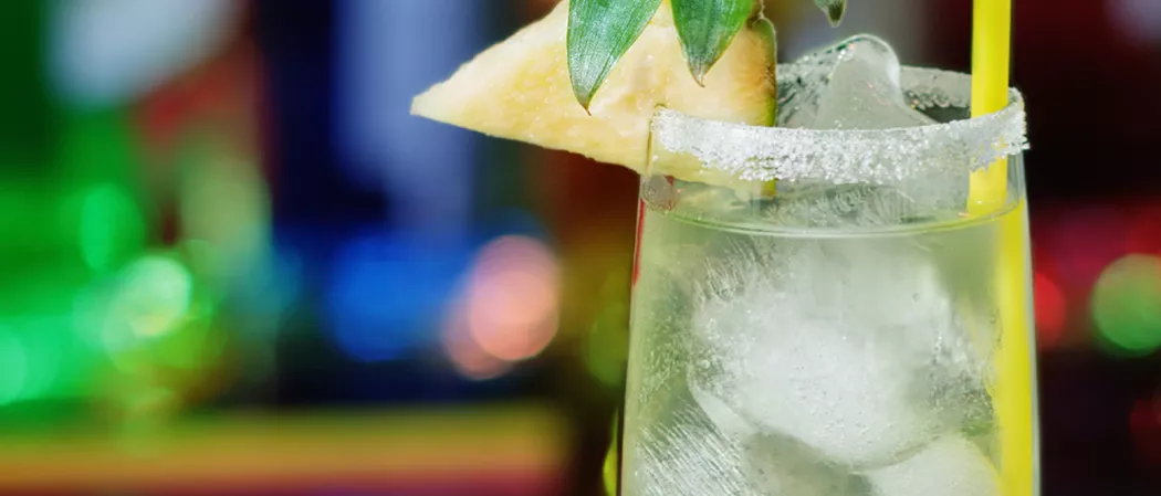 Glass of Midori® and Ginger with ice and a straws, garnished with a pineapple wedge and a salt rim.