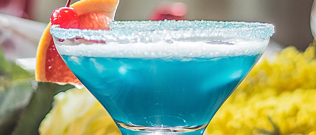 A cocktail glass of Sauza® Blue garnished with blood orange slice and cherry with crushed sugar rim.