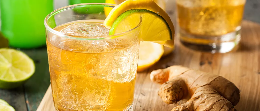 A Glass of Mexican mule garnished with yellow/green lemon slices on glass rim and ice cubes inside along side ginger placed on wooden table