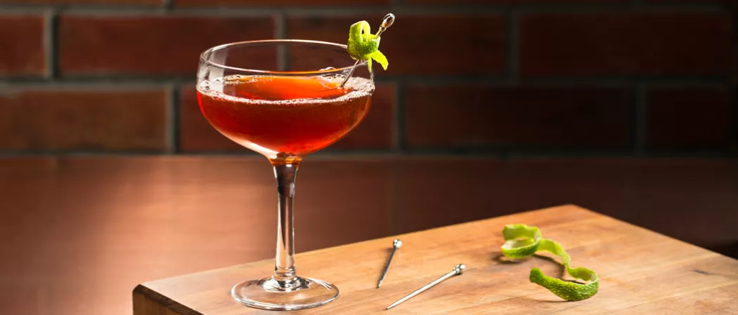 Glass of Jim Beam Orleans garnished with a lime twist, alongside another lime twist and two swizzle sticks.