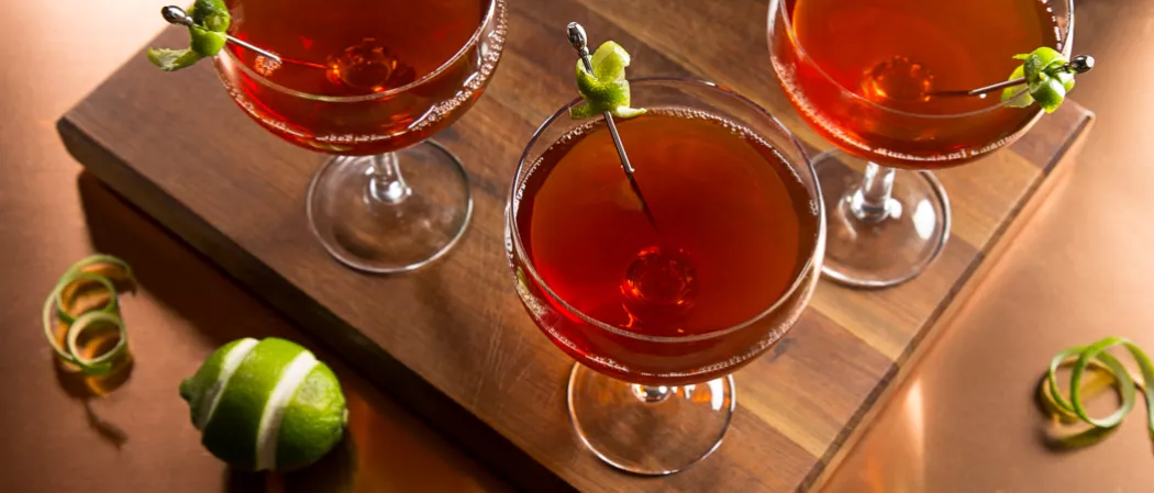 Three Jim Beam Orleans glasses on a tray, each with lime twist garnish, accompanied by an extra lime twist and a peeled lime
