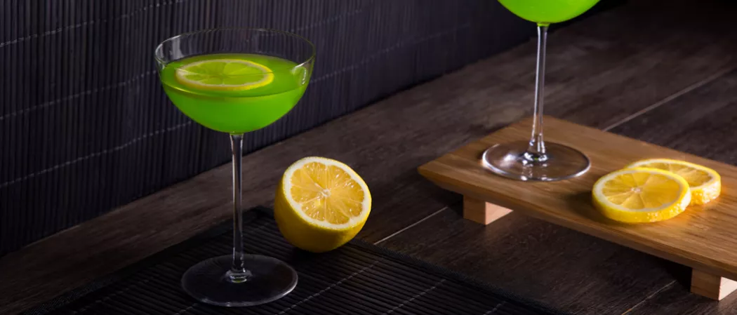 Glass of Holly Jolly garnished with lemon slice alongside half lemon and two lemon slices on wooden board