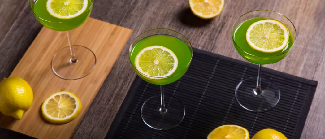 Three Glass of Holly Jolly garnished with lemon slice one on wooden board alongside lemon slice